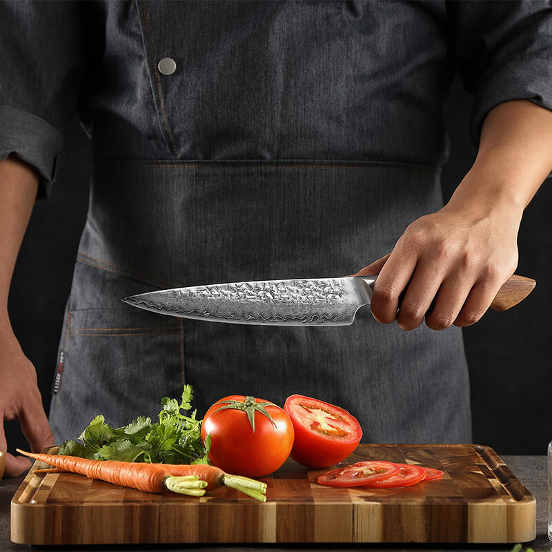 Koch schneidet in der Küche mit Gemüsemesser Tomaten und Karotten in hauchdünne Scheiben aufgrund der harten Klinge des Damastmessers