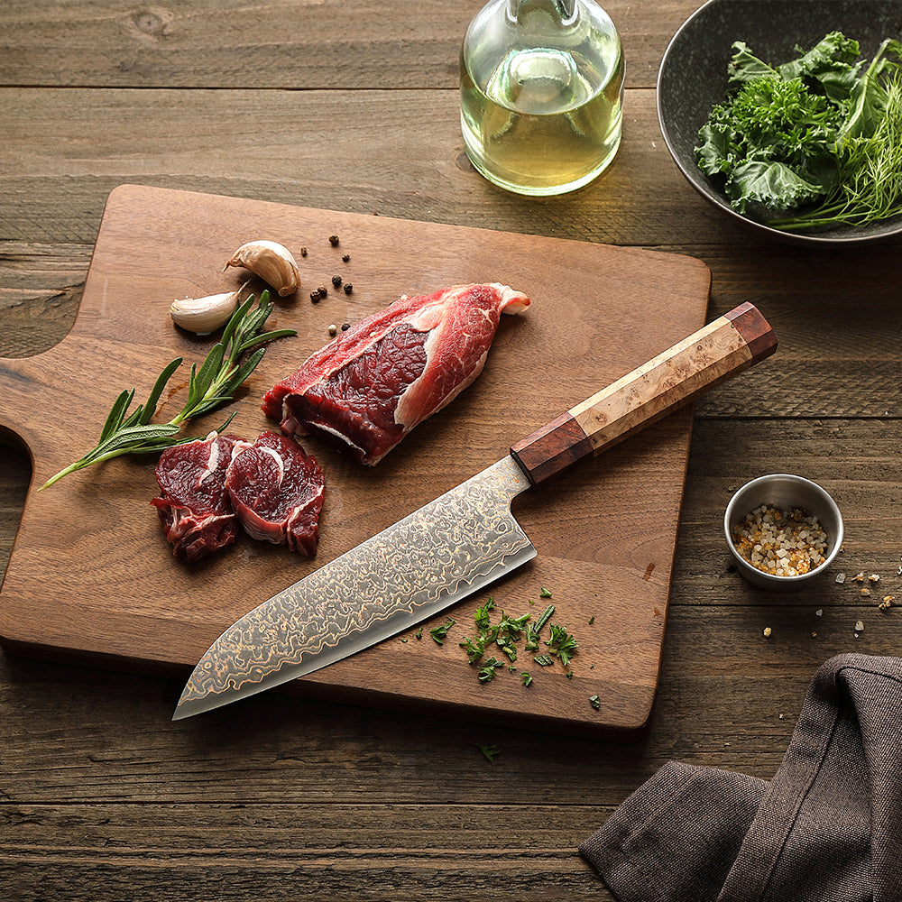 Santokumesser Damastmesser mit gemustertem Klingenblatt und Holzgriff liegt auf einem Holzbrett neben rohem Fleisch, Knoblauch, Rosmarin und Gewürzen.
